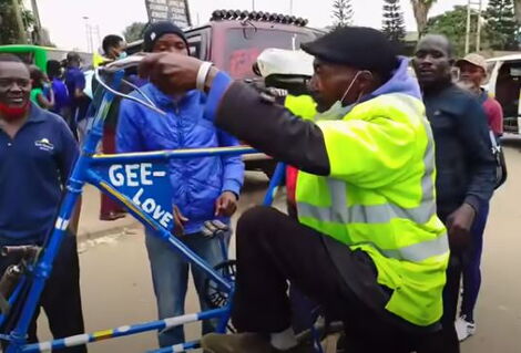 On-lookers watch Mr. Peter Gikiri climbing his bicycle in Allsops, Nairobi on June 4,2021.