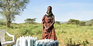 A Turkana lady standing beside a display of shampoo and liquid soap on sale.