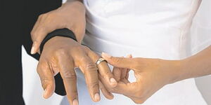 A bride slips a wedding ring on the groom’s hand.