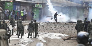 A civilian hurls a teargas canister at anti-riot police.