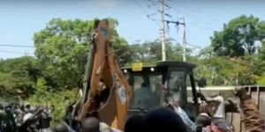 A crowd cheers as a tractor demolishes a business center in Kisumu City