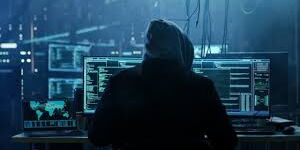 A hacker wearing a hoodie operates a computer