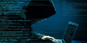A hacker wearing a hoodie operates a computer