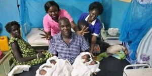 A man holding two sets of twins, his two wives seat beside him and two nurses standing
