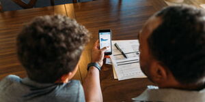 A middle-aged man sits at his dining room table with his young son teaching him about home finances