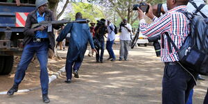 A police officer prepares to launch a teargas canister as journalists take photos. 36 journalists have been attacked in the line of duty between January and April 2020.