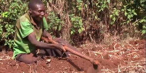 An Image of Simon Chege Digging a Piece of Land While Seated