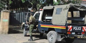 An armed Kenya police officer steps out of a police car.