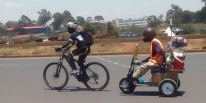 Cyclist Jack Siro pulling a man on a wooden tricycle on Waiyaki Way Thursday October 13, 2022