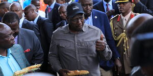 President William Ruto (in black cap) and Deputy President Rigathi Gachagua chew roasted maize during a conversation with traders moments before the official launch of the Hustlers Gund on November 30, 2022. 