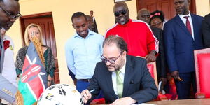 Austrian Ambassador Christian Fellner signs visitors book during the launch of Acakoro Football Academy in Homa Bay County on Tuesday, March 21, 2023.