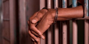 Hands resting on jail bars at a police station.