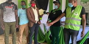Kelvin Mwangi Maina (center) receives his certificate of clearance from IEBC Returning Officers Faith Mugo (second right) and Stephen Gitau (right) on October 16, 2020.