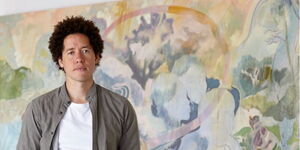 Kenyan artist Michael Armitage standing next to one of his paintings