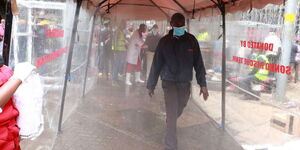 Nairobi residents use a sanitiser spray booth installed by the Sonko Rescue Team at the Kencom bus stage, April 19, 2020.
