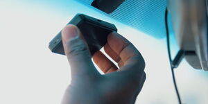 Driver holding OBU device on car's windscreen