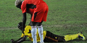 Former Harambee Stars player Crispin Olando (in red shirt) helps a Uganda Cranes player back on his feet during a match played in October 2011