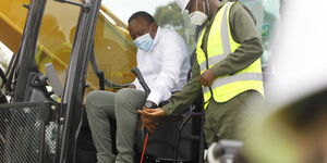 President Uhuru Kenyans (in white shirt) is shown how to operate construction machinery by a worker