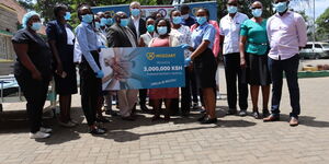 Pumwani Staff and Mozzart Bet team pose for a photo with the dummy cheque representing the sum of the donation.
