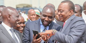 President Uhuru Kenyatta using a phone with Senator Kipchumba Murkomen as Deputy President William Ruto watches 
