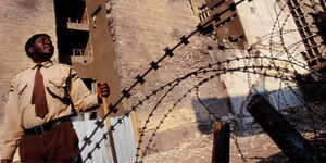 A security guard watches over the remains of the United States embassy, after the bombing