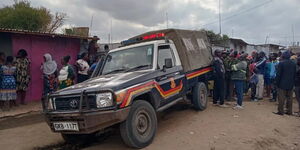 Residents surrounding a police land cruiser at a past crime scene