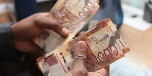 A man counting several one thousand Kenyan shillings bills.