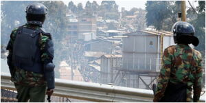 Anti-riot police officers overlook protesters from a vantage point.
