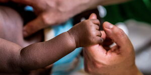 A newborn baby grips a mother's hand 