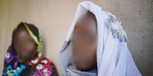 Close up portrait of sad African girls with traditional clothing sitting by a wall.