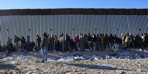 Migrants gather along the border wall Tuesday, Dec. 5, 2023, in Lukeville, Arizona.