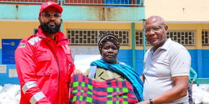 Safaricom Foundation Chairman Joe Ogutu(Right) and Secretary General, Ahmed Idris (left) hands over food hamper and blankets to Peris Odhiambo(Center) during the M-Pesa Foundation flood response and food distribution in Kibera.