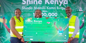 Safaricom PLC, TBL, Kaimbu Elizabeth Kinyanjui (L) and Frontline Marketing Operations, Julius Kamotho awarded Mary Chege, the first draw winner of Shine Kenya, a dummy check for Ksh.1,000,000 in Kasarani, Carwash.