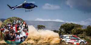 A photo of a helicopter monitoring a safari rally car in 2021 in Naivasha and rally enthusiasts at the event held on June 27, 2022.