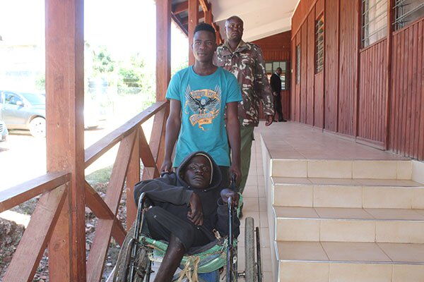 Peter Dues pushes Emanuel Masabuko's wheelchair as they are accompanied by a police officer. The two were arrested in Bomet for being in the country illegally on Monday, September 30.
