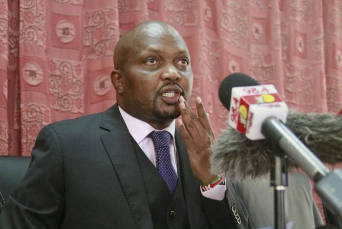 Moses Kuria addresses the press from parliament buildings at a past event.