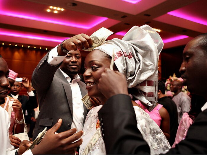 A Nigerian bride participating in the money dance as guests spray money on her.