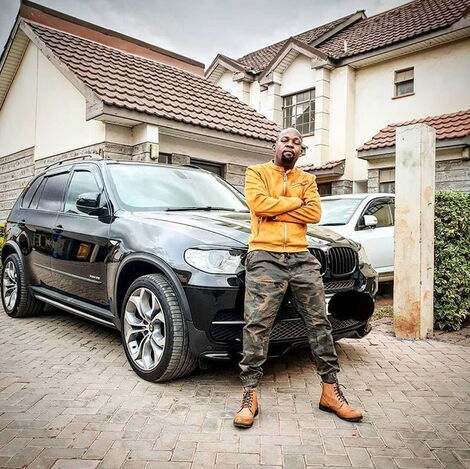 An undated image of Alex Mwakideu posing for a photo in front of his house.