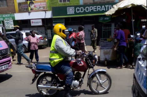 A boda boda rider vrooms past a building with Cooperative Bank signage