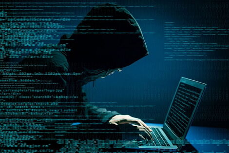 A hacker wearing a hoodie operates a computer
