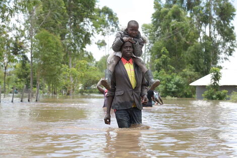 A man crosses through floodwaters in Nyando on Tuesday, April 21, 2020, while carrying a child.