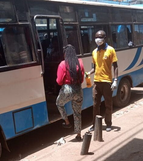 A tout stands watch at the matatu doors armed with a hand sanitizer, sterile gloves and a mask.