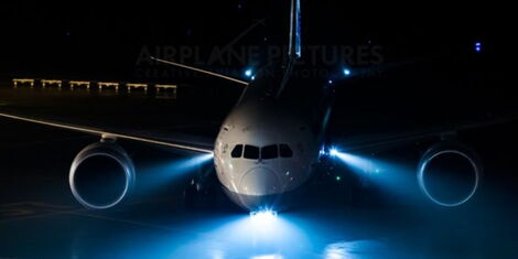 An aeroplane with its light turned on at an airport.