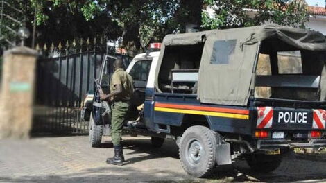 An armed Kenya police officer steps out of a police car.