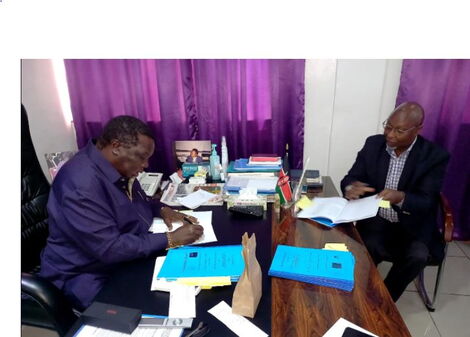 COTU Sec-Gen Francis Atwoli (left) inks a salary increament deal in the presence of a guest on Monday, November 1, 2021.