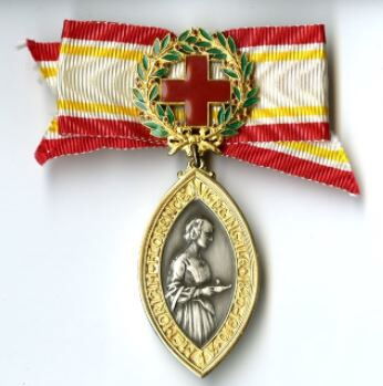 A Florence Nightingale Medal made with a ribbon with colours red, green and yellow on it. The medal is made of a metal.