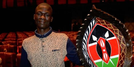 Collins Ouma who was accused of violently robbing a police officer holding up a shield with Kenyan colours