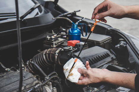 An image of a motorist wiping a dipstick used to check oil levels in a car.