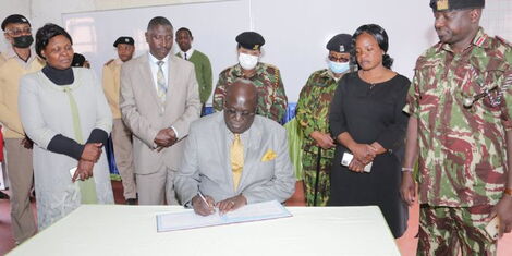 Education CS George Magoha signs a visitor's book after commissioning CBC classrooms at the Alliance High School on Sunday, July 31, 2022.