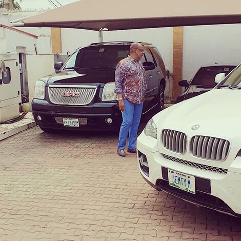 Emmy Kosgey's husband, Apostle Anselm Madubuko, poses for a photo alongside a BMW and an SUV on Friday, March 6, 2020